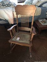 Front view of vintage wooden rocking chair showing carved backrest with spindles and upholstered seat.
