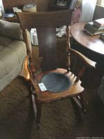View of the vintage wooden rocking chair showing shapely backrest, armrests, and round embossed fiber board seat attached with tacks.
