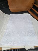 Close-up view of several white and off white textile place mats with decorative raised floral and geometric patterns.