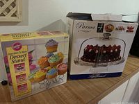 Photo showing boxed Wilton Cupcakes N More dessert stand and Parma glass covered cake stand box