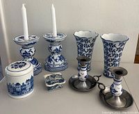 Front view of eight blue and white pottery pieces including candlesticks, vases, jar, and trinket box arranged on a white surface.