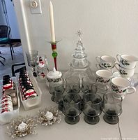 Full display of lot items arranged on table including mugs, glasses, napkin rings, candy canes, candlesticks, glass Christmas tree centerpiece, and decorative candle holders.