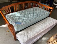 Photo of wooden day bed with main pale blue floral pattern mattress and slide out white trundle mattress underneath, shown partially pulled out.