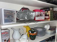 Photo of shelf displaying Disney Cars metal cake pan, boxed cake decorating kits, salad spinner, pitchers, plastic drawers, and kitchen utensils