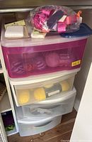 Plastic drawers with yarn skeins and a clear bag of pink ribbons on top