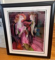 Framed artwork showing the entire piece including black frame and white matting, featuring two stylized figures with the woman in a pink gown.