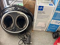 Black Snailax Shiatsu foot massager with dual foot openings, control dial with mode and heat button on top, showing power adapter cord in garage setting