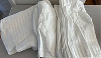 White queen-size mattress protector and two white flat sheets with different textures folded on a surface.