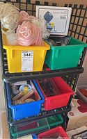 Photo showing multiple colored plastic bins on black shelving containing yarn and crafting supplies including yarn balls and packaged sewing tools.