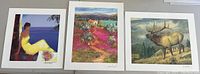 Three seriolithograph prints laid side by side showing different scenes: a woman by the sea, a colorful landscape with a house near the lake, and an elk in the woods.