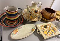 Assorted stoneware and pottery serving pieces including pitchers, bowls, vegetable dish and plates with floral and striped designs