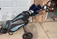 Photo showing the full golf set including the golf bag on a three-wheeled rolling golf trolley, multiple golf clubs with headcovers inside the bag.