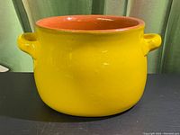 Side view of the yellow ceramic flower pot showing the round shape, side handles, and glossy finish.