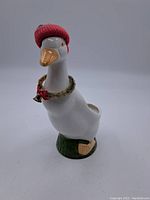 White ceramic duck figurine with a red knitted hat and tinsel collar with a bell, standing on a green base.