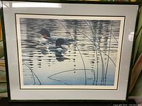 Framed print showing two Common Loons on water with reeds, signed at bottom right by Don Leger.