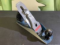 Front angle of the Stanley hand planer showing metal body, blade adjustment cover with red logo, and black front knob.