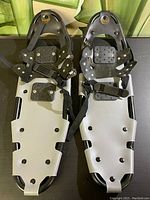 Full view of both Kuiet snowshoes showing black metal frames, gray plastic decking, and adjustable black foot straps.