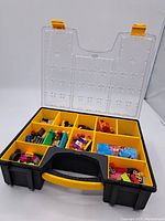Open black and yellow plastic carrying case showing LEGO bricks sorted into compartments under clear lid with yellow latches