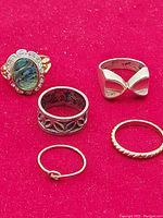Five rings on red cloth showing variety of designs, stones, and metals