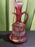 Pink glass decanter standing upright, showing front and side views with a stopper.