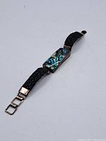 Full view of sterling silver bracelet with turquoise centerpiece and braided black leather strap laid flat on white background.