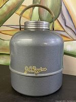 Front and angled view of the vintage J.C. Higgins camping water thermos in metallic gray with logo and metal handle.