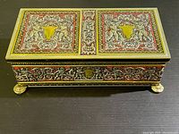 Front angled view of the rectangular ornate incense holder box showing intricate detailing on the lid and brass-like feet.