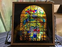 Full view of the miniature stained glass panel in wooden frame with light shining through.