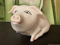 Front and side view of a vintage light pink ceramic piggy bank lying down with detailed eyes and pink accents.