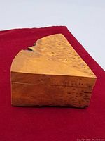 Side view of triangular wooden trinket box showing wood grain and natural knot on the lid.