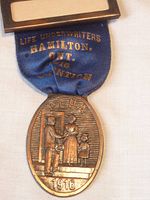 Full view of the pin showing the ribbon with gold text and bronze medallion with figures and year 1916