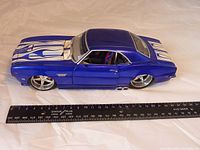 Top view of 1968 Chevrolet Camaro Z/28 die cast model showing blue body with white flame decals and chrome wheels. Ruler included for size reference.
