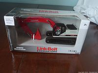 Front view of boxed Link-Belt 210X3 excavator die-cast model showing red excavator arm, black and white cab, and branded packaging.