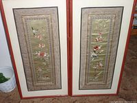 Two Asian embroidered tapestry panels framed in bamboo style frames, showing detailed embroidery with flowers and birds on silk fabric.