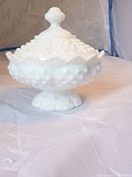 Fenton Hobnail milk glass candy dish with covered lid on a white surface, showing the side profile and hobnail texture.