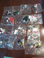 Photo showing 14 sealed bags each containing assorted Lego pieces including bricks, wheels, minifigure parts, and accessories. The bags vary in content and piece types.