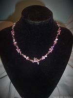 Necklace displayed on a black velvet bust showing pink rhinestones along the chain.