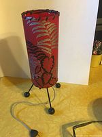 Full view of vintage red table lamp with fern and leaf pattern, metal tripod base, unplugged.