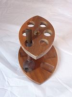 Photo showing wooden eye-shaped pipe stand with one pipe inserted and multiple empty circular and groove slots