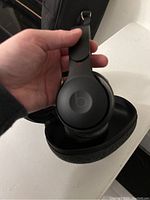 Black Beats wireless Bluetooth headphones held over the open carrying case.