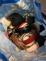 Top down photo showing a collection of various belts including braided brown, red, black, pink, and cream colored belts inside a blue reusable shopping bag.