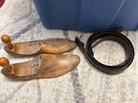 Pair of antique hinged wooden shoe stretchers with natural wood finish and two large rolled brown leather belts with brass buckles.