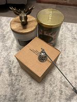 Three large candles: white ceramic with moose lid, green 'Holiday Spice' candle, and boxed candle along with metal candle snuffer.