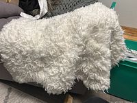 Cream colored faux sheepskin rug shown draped over sofa, highlighting texture and color.