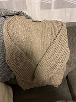 Beige cable knit sweater laid out flat showing overall knit pattern and shape.