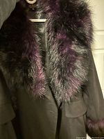 Close-up of the fur collar in purple and black on the black coat, showing texture and colors.