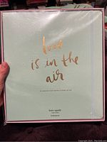 Front of the Kate Spade bridal planner showing the soft mint cover with gold foil text 'love is in the air', sealed in plastic wrap.