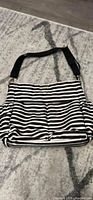 Front view of the diaper bag showing black and white horizontal stripes and single adjustable black shoulder strap.