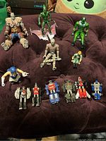 Overview of assorted action figures on a dark soft surface featuring humanoid characters and five Transformers G1 cassette robots in front.
