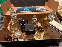 Box containing multiple assorted perfume bottles including clear fluted stoppers and black capped rectangular bottle